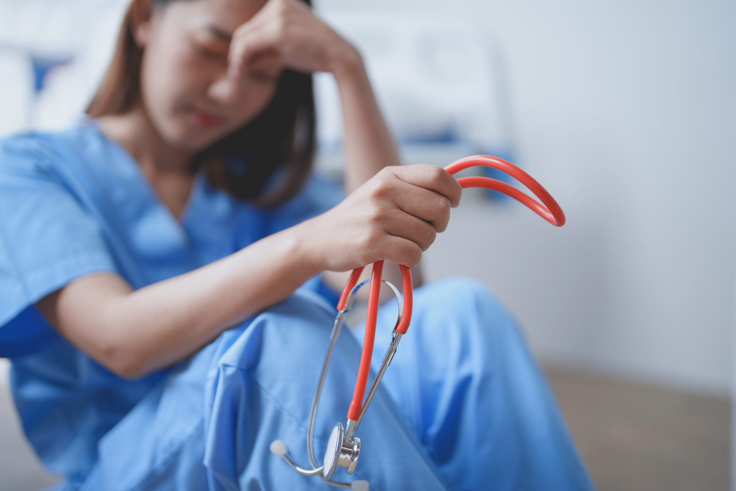 Young female doctor in blue scrubs is feeling overwhelmed and stressed while sitting on the floor in a hospital room